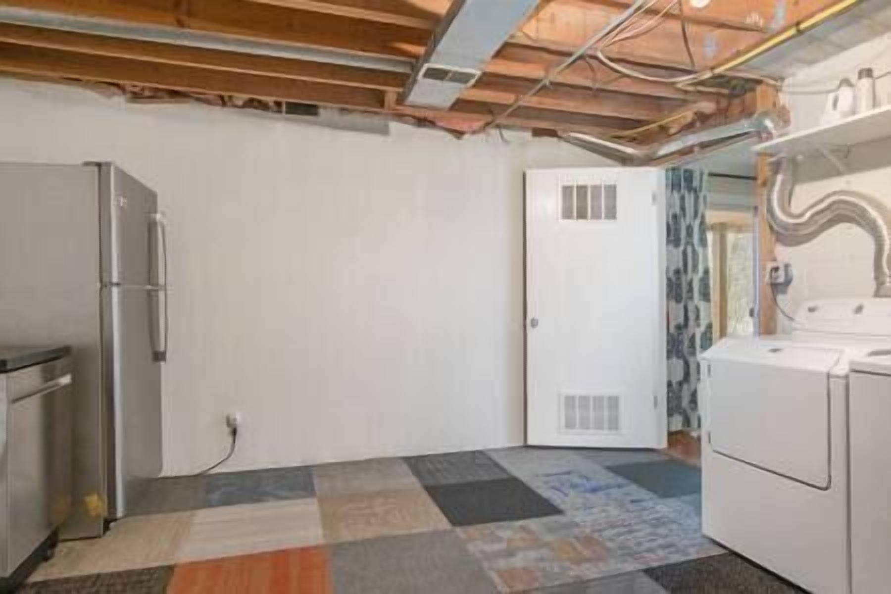 Una cocina con refrigerador, lavadora y puerta que da a otra habitación.