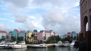 A marina with several boats docked, colorful buildings in the background, and a prominent arch structure on the right. - Spend your holiday in Paradise (Paradise Island)