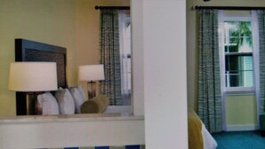 A hotel room with a bed, a desk with a lamp, a window with curtains, and a ceiling fan. - Spend your holiday in Paradise (Paradise Island)
