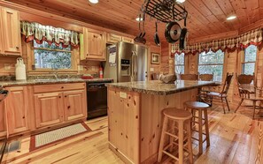 A wooden cabin-style kitchen with granite countertops, wooden cabinets, a stainless steel refrigerator, and a hanging pot rack.
