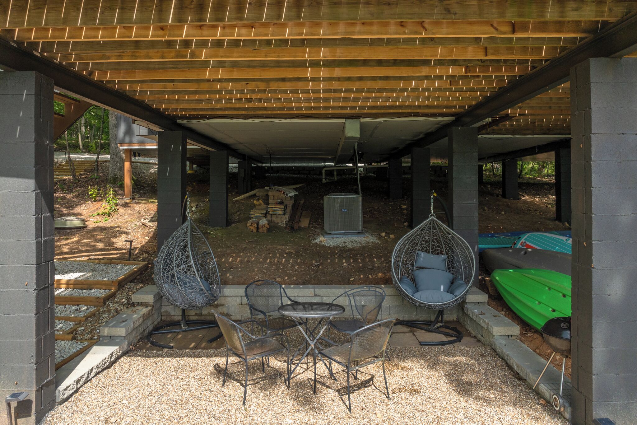 An outdoor covered patio with a table and chairs, a hanging chair, and a kayak.