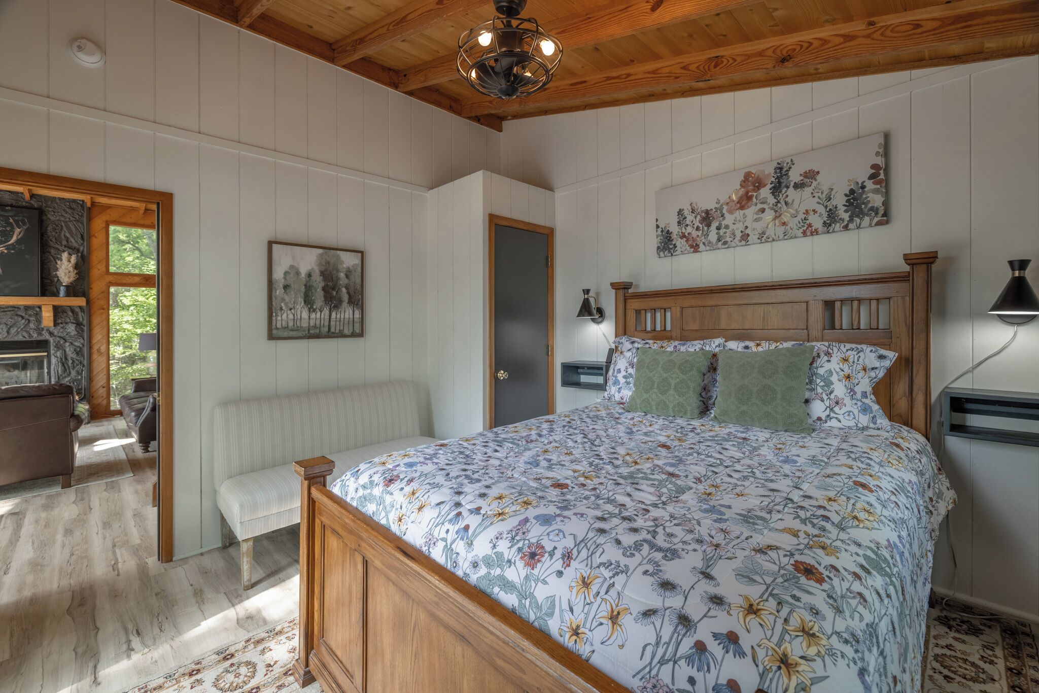 A bedroom with a wooden bed, a bench, a radiator, a door, and a wall with a floral painting.