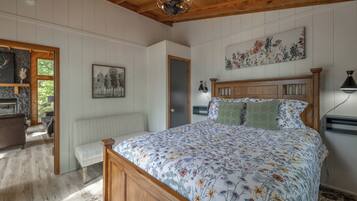 A bedroom with a wooden bed, a bench, a radiator, a door, and a wall with a floral painting.