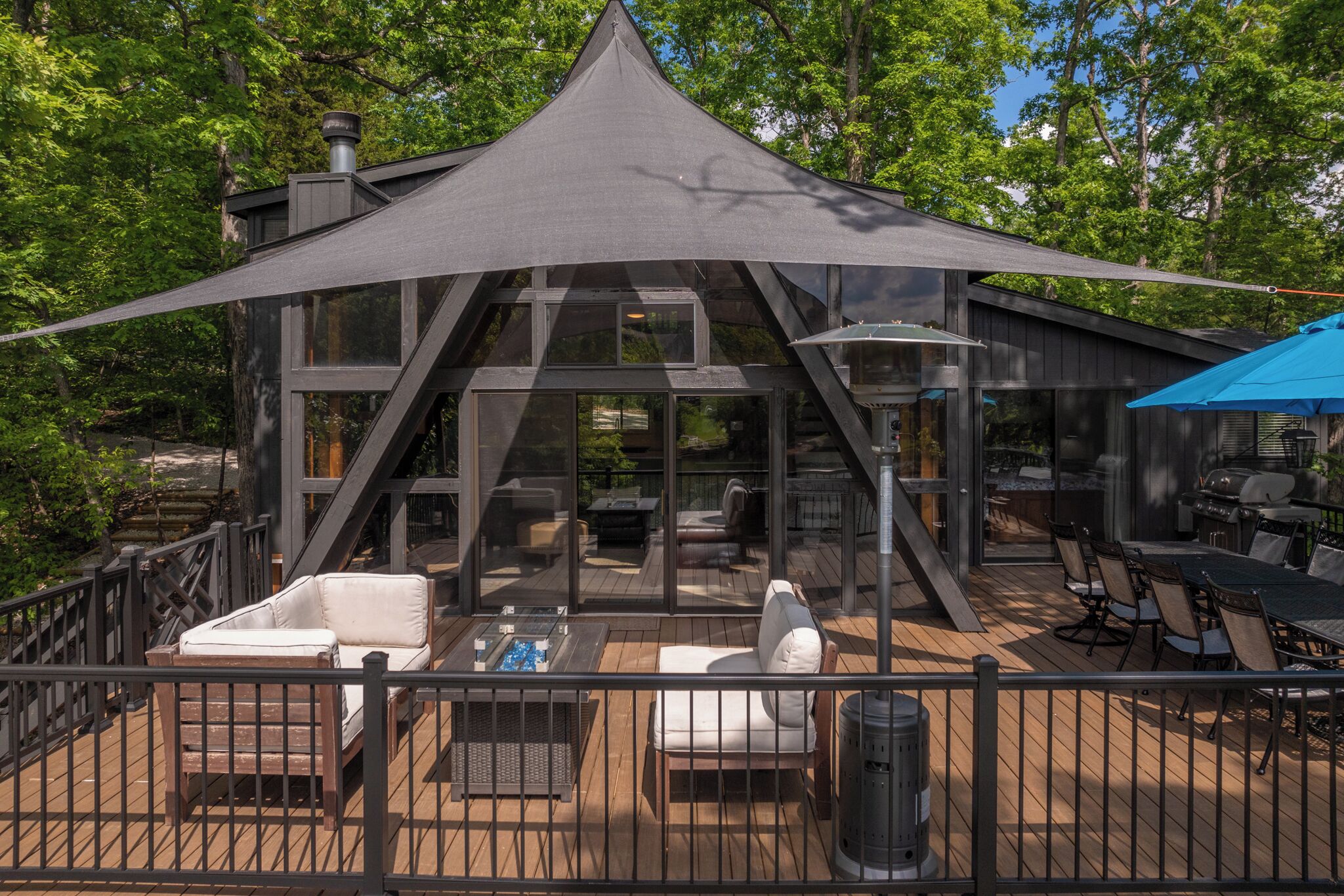 A modern house with a large deck, outdoor seating, and a barbecue area.