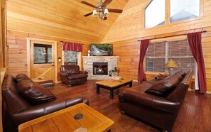 L’intérieur chaleureux d’un chalet avec des murs en bois, une cheminée, des canapés en cuir et une table à manger.