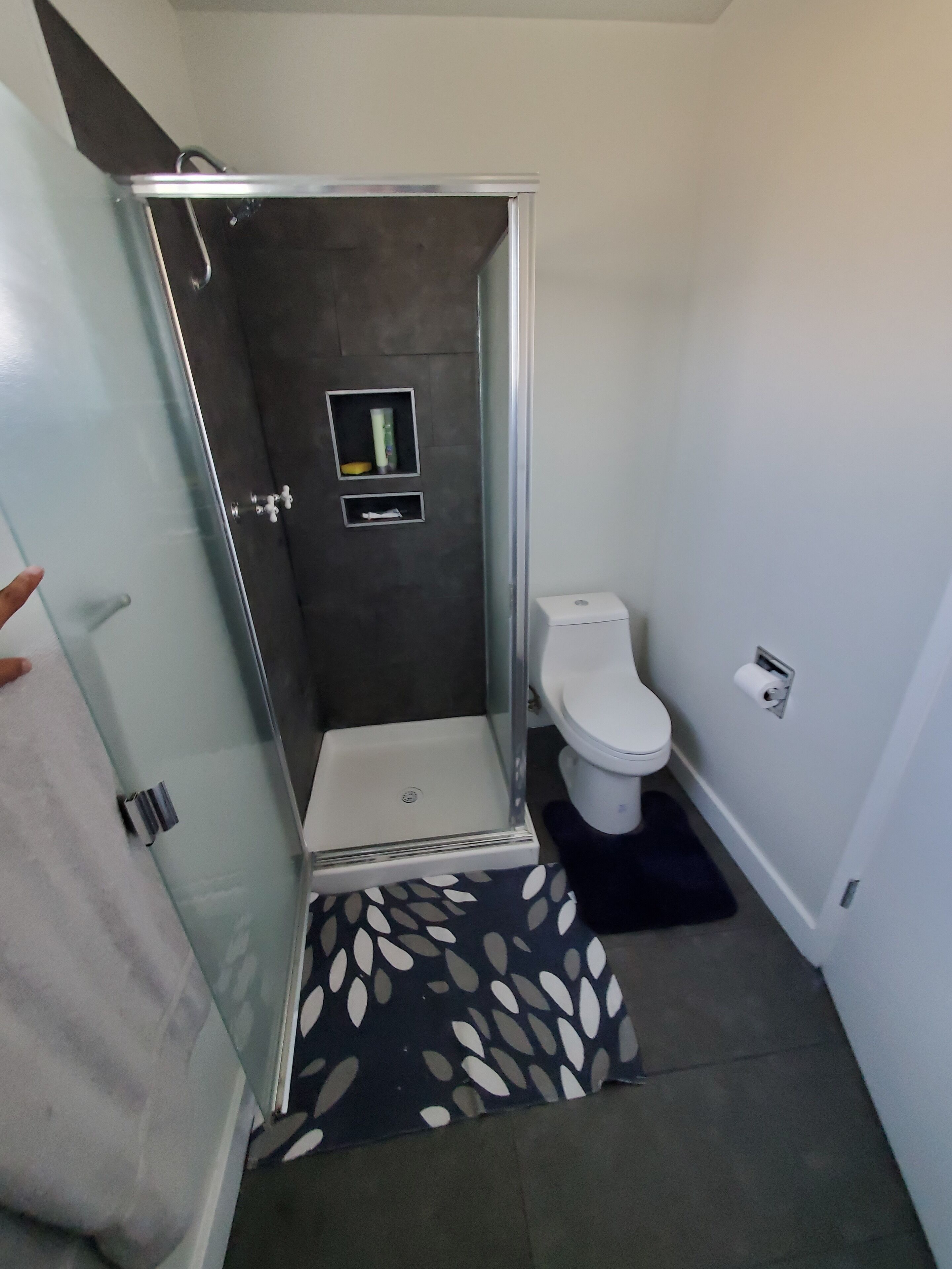 Ein Badezimmer mit einer gläsernen Duschkabine, einer Toilette und einer kleinen Ablage mit Pflegeprodukten.
