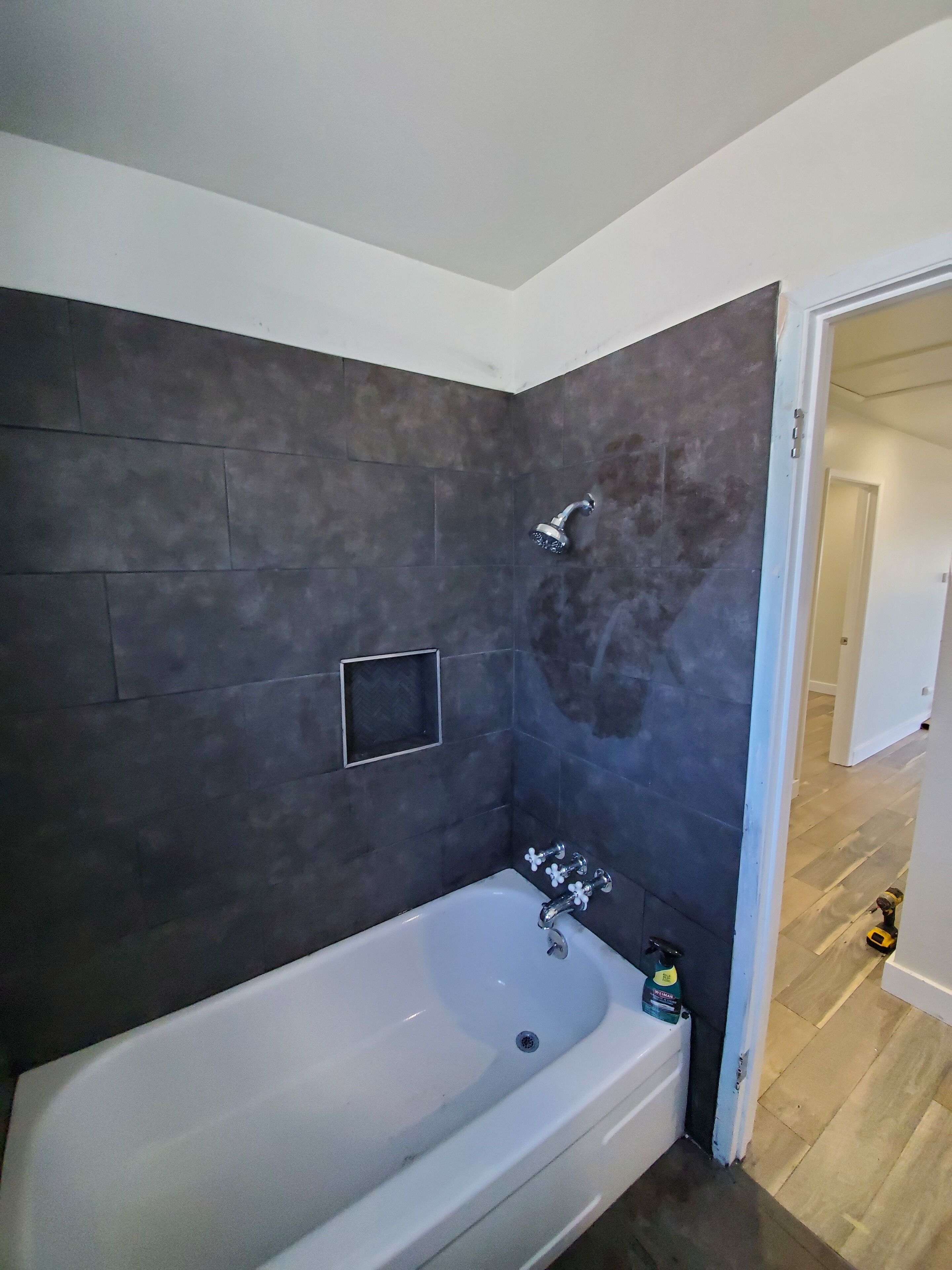 Ein modernes Badezimmer mit einer großen Badewanne, dunklen Fliesenwänden und einer sichtbaren Duschbrause.