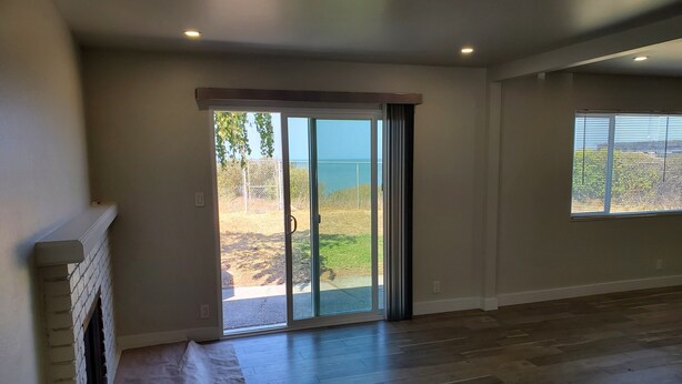 Una habitación amplia con un gran ventanal corredera que da a un patio, una chimenea y una ventana con persianas.