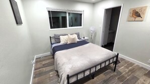 Un dormitorio con cama, ventana, ventilador y un cuadro en la pared.
