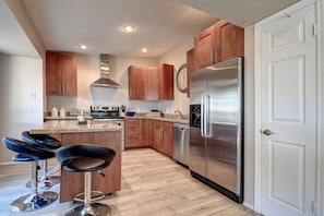 A modern kitchen with wooden cabinets, stainless steel appliances, and a bar area with stools.