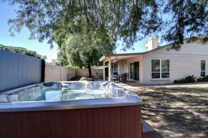 A hot tub in a backyard with a covered patio and a house in the background.