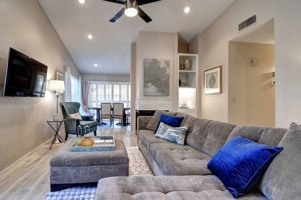 A living room with a grey sofa, ottoman, and a dining area with chairs and a table.