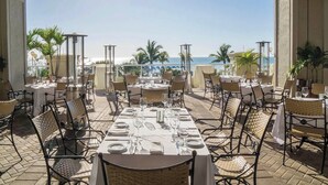 An outdoor dining area with tables set for two, overlooking a beach. - Suite on the beach, classy, large private patio (Marco Island)