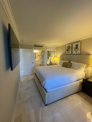 A hotel room with a large bed, bedside lamps, a flat-screen TV mounted on the wall, and framed botanical prints above the bed. - Suite on the beach, classy, large private patio (Marco Island)