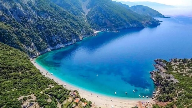 Un paisaje costero con playa, aguas cristalinas y vegetación circundante.