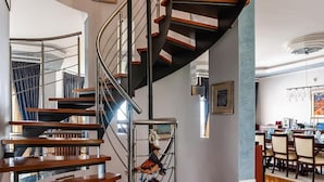 Una escalera espiral moderna con peldaños de madera y barandillas de metal, que conduce a un piso superior.