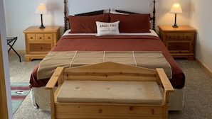 A bedroom with a wooden bed, two bedside tables with lamps, a ceiling fan, and a wall-mounted painting.