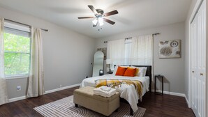 A bedroom with a bed, a ceiling fan, a window with curtains, a bedside table, and a wall-mounted mirror. - The Red Door Retreat: Where Wellness Meets Southern Hospitality ✨ (Atlanta)