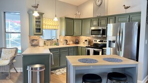 Una cocina moderna con armarios verdes, electrodomésticos de acero inoxidable, una isla central con taburetes y adornos de gaviotas en la pared.