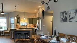 Una cocina moderna con armarios verdes, una isla central y un comedor con una mesa de madera dispuesta para cuatro.