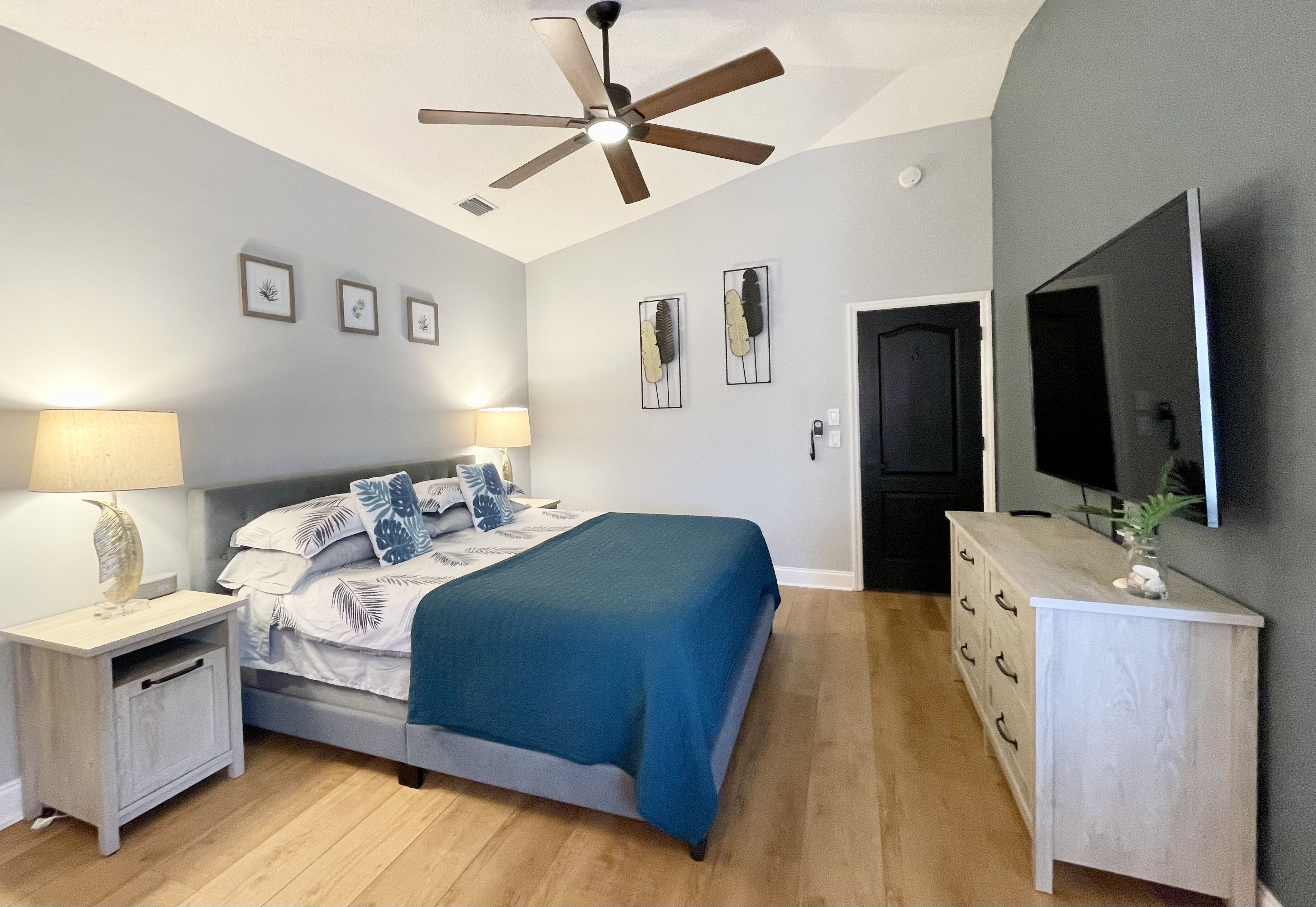 A bedroom with a bed, nightstands, a dresser, a ceiling fan, and a TV.