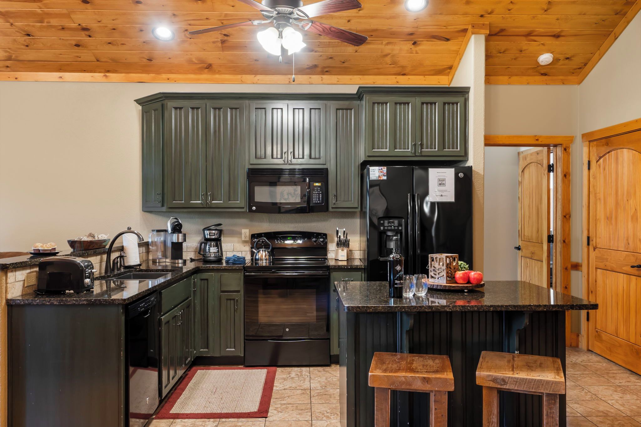 A kitchen with dark green cabinets, a microwave, a refrigerator, a coffee maker, and a toaster.