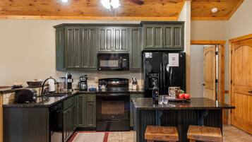A kitchen with dark green cabinets, a microwave, a refrigerator, a coffee maker, and a toaster.