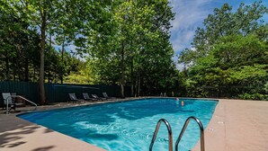 Ein rechteckiger Pool mit glasklar blauem Wasser, umgeben von einer Betonplattform. Auf der rechten Seite sind Metallpoolleiter und am linken Rand eine Reihe leerer Liegestühle zu sehen.