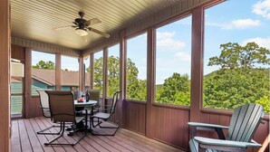Eine überdachte Terrasse mit Tisch und Stühlen, großen Fenstern und einem Deckenventilator.