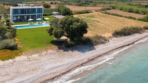 A modern house with a swimming pool, surrounded by a landscaped garden and a beach.