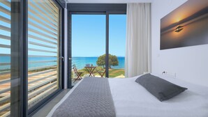 A bedroom with a bed, a painting, and a view of the beach.