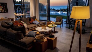 A modern living room with a sofa, coffee table, and lamp, overlooking a scenic view of the ocean.