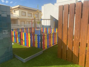 Un espace de jeux clôturé, agrémenté de panneaux colorés et doté d’une porte en bois.
