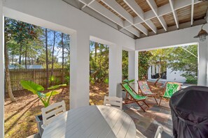 A covered patio with a table and two lounge chairs, surrounded by a wooden fence and lush greenery.