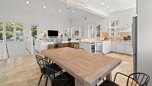 A spacious kitchen with white cabinetry, a wooden dining table, and a modern chandelier.