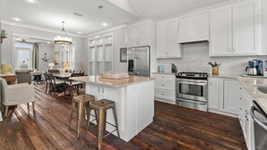 A modern kitchen with white cabinets, stainless steel appliances, and a wooden floor.