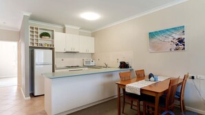 A compact kitchen with a dining area, white cabinets, a microwave, and a small island. - Apollo Quays Apartment (Halls Head)