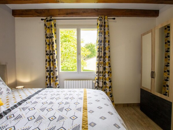 A bedroom with a bed, a window with curtains, a radiator, and a wardrobe.