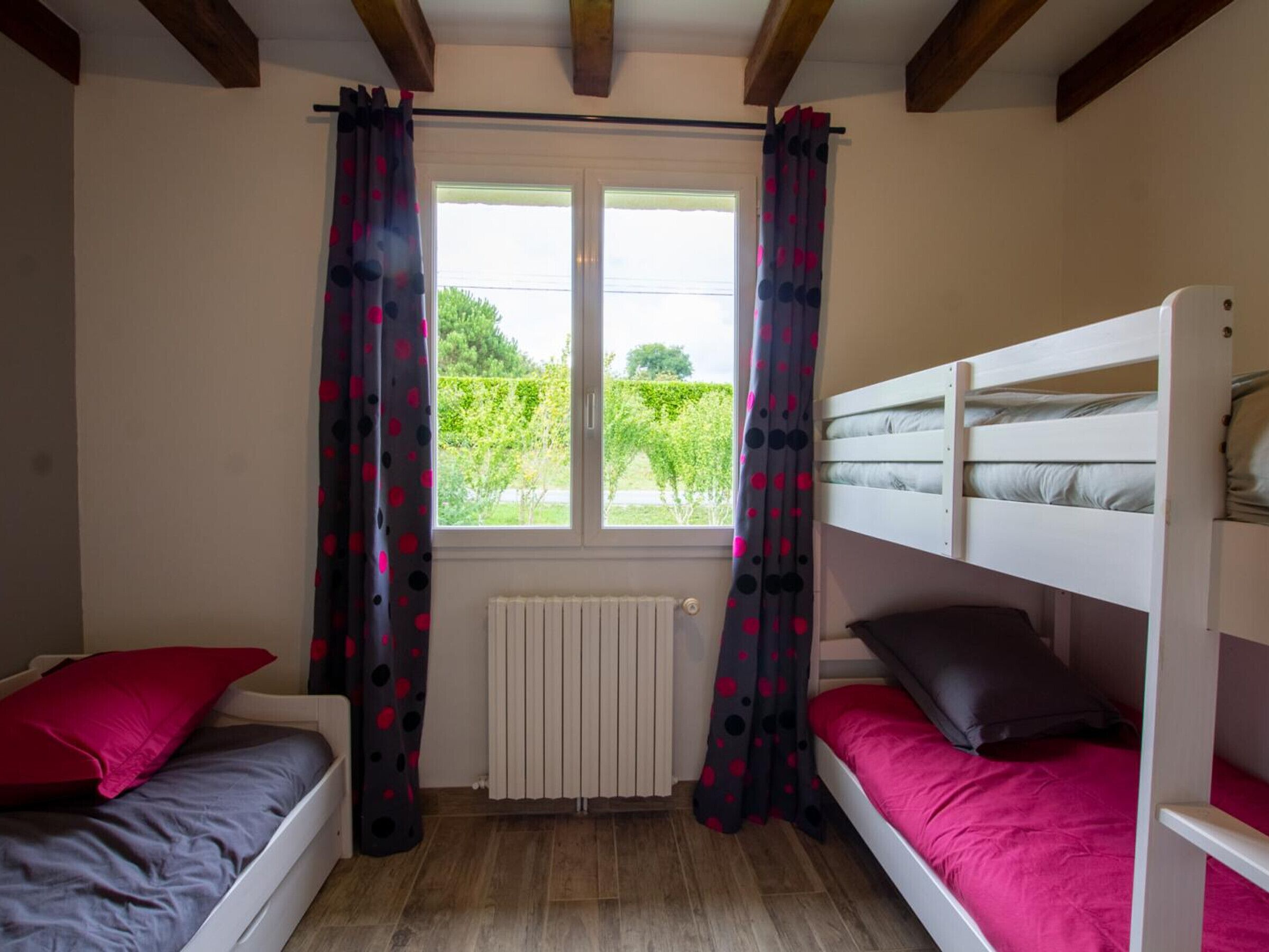 Una habitación con dos literas, una ventana con cortinas, un radiador y vistas a zonas verdes.