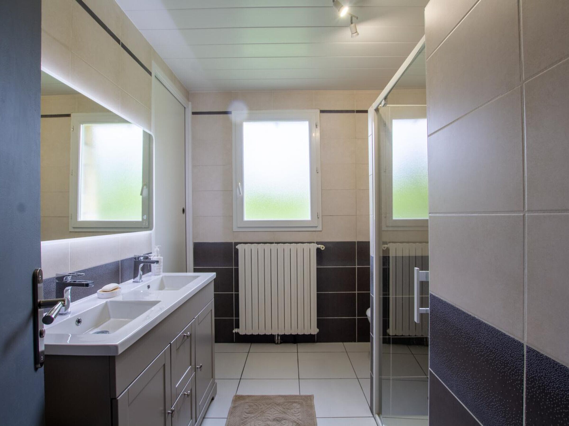 Un baño moderno con tocador doble, zona de ducha y ventana que proporciona luz natural.
