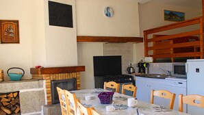 A dining area with a table set for four, surrounded by wooden chairs, a fireplace, a stove, and a kitchen area with a microwave and refrigerator.