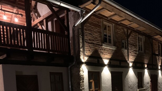 Ein Gebäude mit einem hölzernen Balkon und einer Ziegel-Fassade, beleuchtet von Außenlichtern.