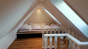 Ein kleines Schlafzimmer im Dachgeschoss mit schrägen Wänden, Holzdielen und einem weißen Geländer.