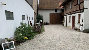 Ein Innenhof mit einem gepflasterten Weg, weißen und Backsteingebäuden sowie einem Holztor.