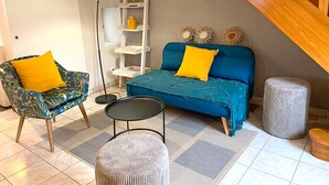 Un salon avec un canapé bleu, un fauteuil à motifs, une petite table ronde et un grand lampadaire.