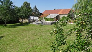 Un bâtiment rustique en pierre, avec un toit rouge, une cour verdoyante et un arbre aux pommes vertes.