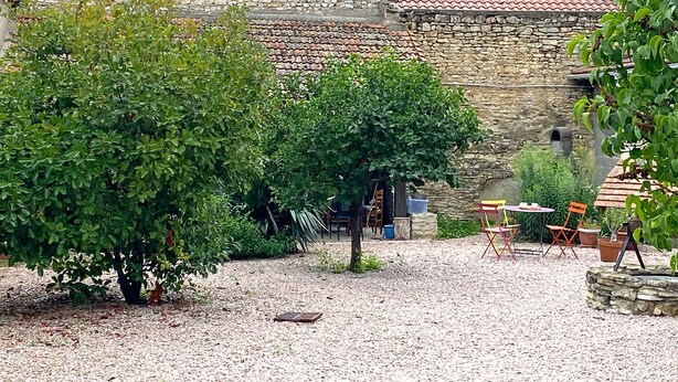 Une cour intérieure avec un mur en pierre, un sol recouvert de gravier et du mobilier d’extérieur.