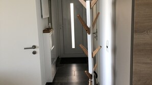 Ein Flur mit einem hölzernen Kleiderständer, einer weißen Tür und einem gefliesten Boden.