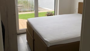Ein Schlafzimmer mit einem großen Bett, einer Schiebetür zu einer Terrasse und Blick auf einen See.