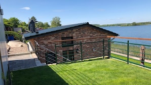 Ein Backsteinhaus mit einem Metallgitter, einer grünen Rasenfläche und Blick auf einen See.